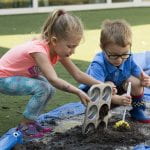 A young boy and girl play in the mud with kitchen untensils.
