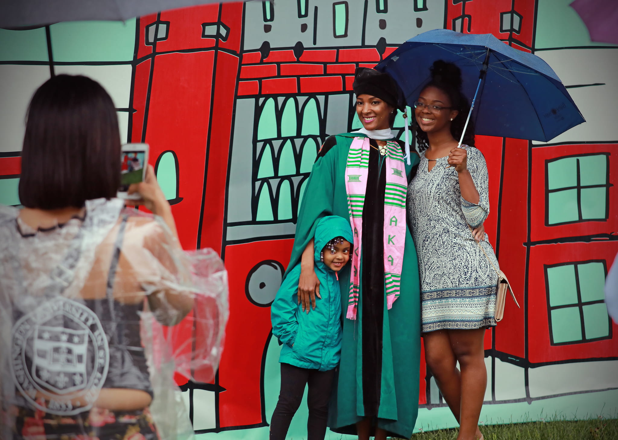 A college graduate, her parent, and young sibling stand in front of a backdrop of Brookings Hall at WashU