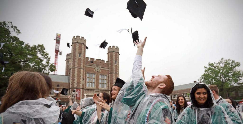 College graduates wearing rain ponchos toss their caps into the air at Commencement
