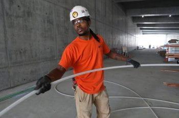 An African-American construction worker handles piping in the interior of a concrete structure.