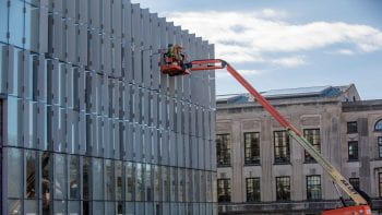 Construction workers are lifted up to the west facade of Weil Hall
